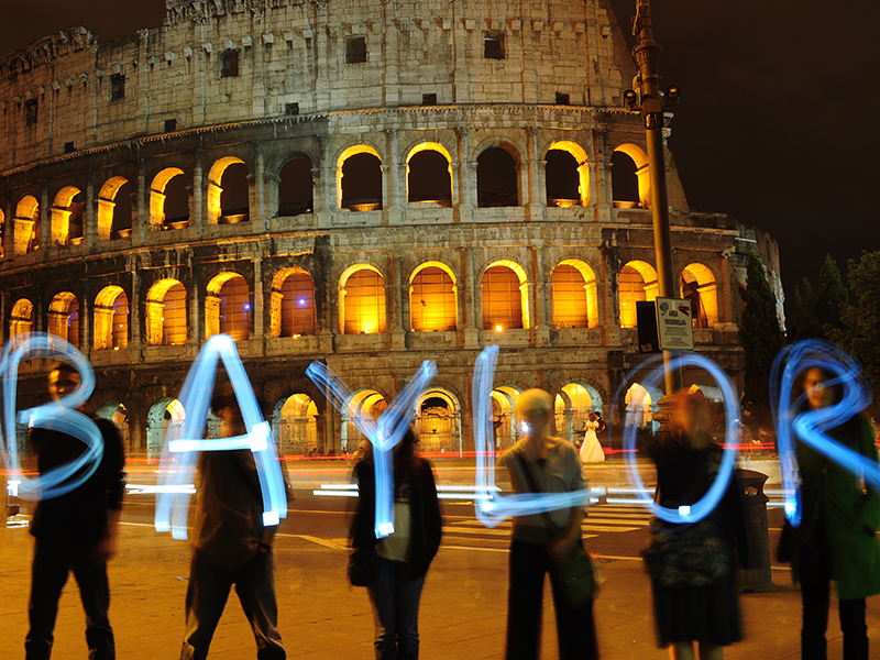 A group of people spelling the word BAYLOR in front of the colosseum.