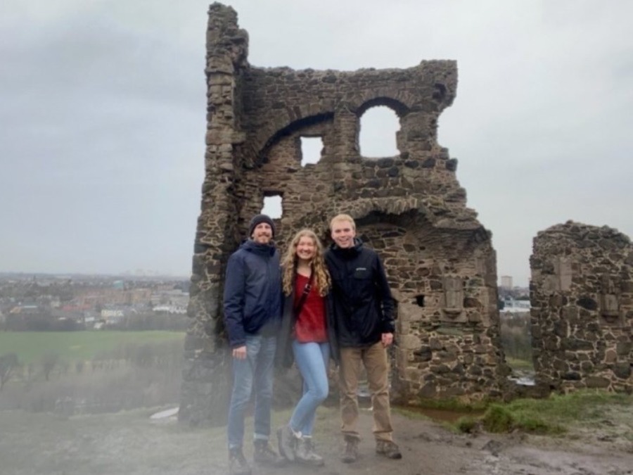 Three people stand in front of ruins.
