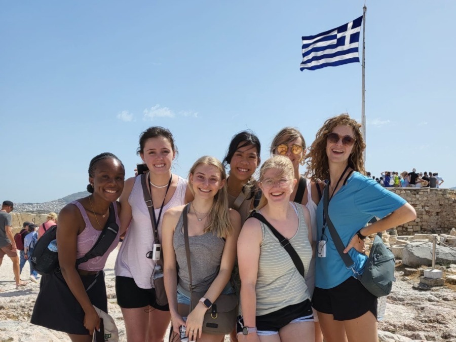 A group of people pose in front of a Greek flag.