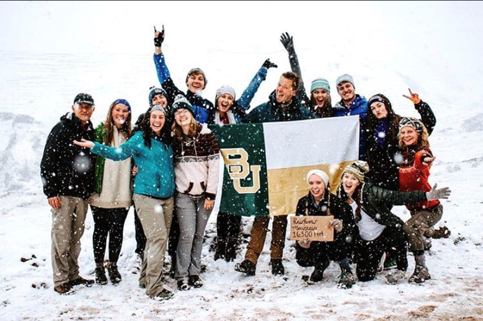 A group of people stand in the snow holding a BU flag.