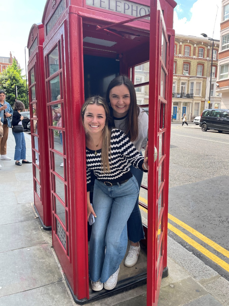 Two people lean out of a red telephone box.