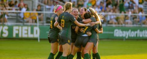 Baylor soccer players hugging on field in front of spectator stands