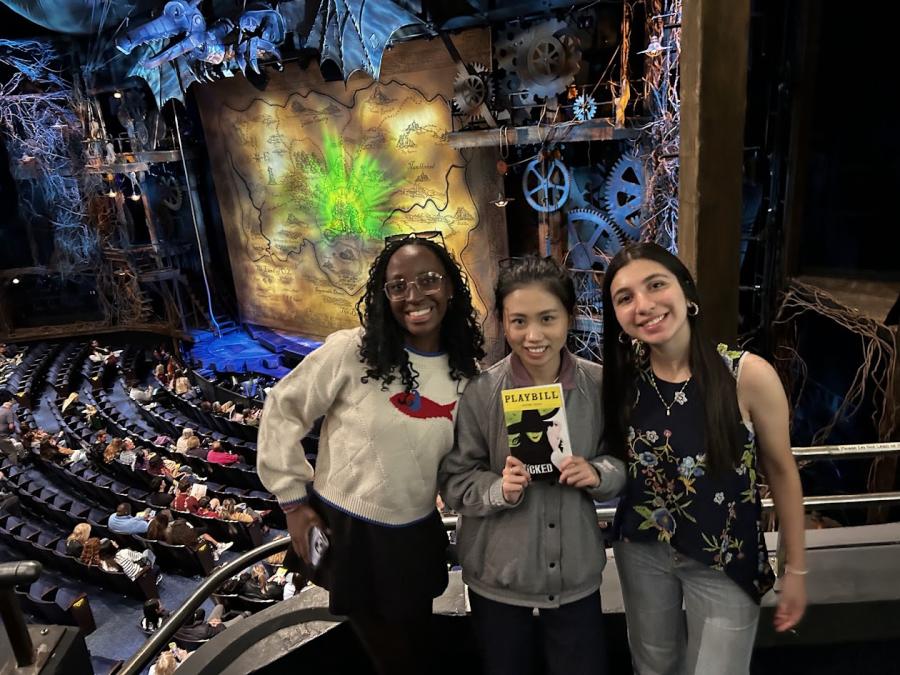 Three international students pose in front of the Wicked Broadway set.